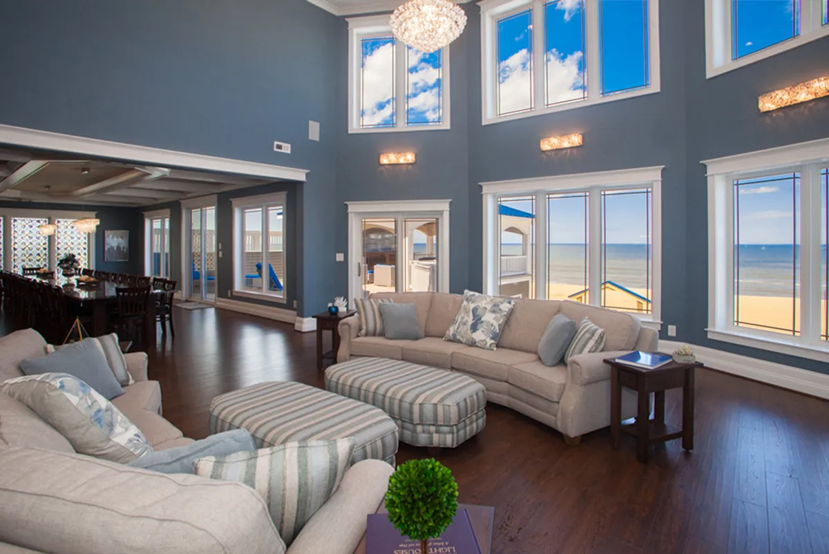 This image features a cozy, open seating area bathed in natural light from large windows. The arrangement of comfortable chairs and a tasteful chandelier creates an inviting atmosphere that's perfect for relaxing with family or entertaining guests. Decorative accents on the walls and a glimpse of an expansive view outside enhance the welcoming vibe.