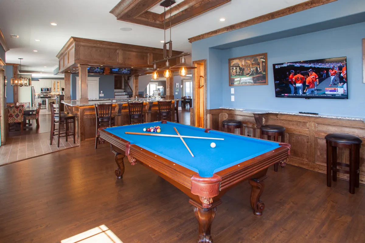 This interior image showcases a vibrant, open area featuring a pool table and a stylish bar area with wood paneling. The setting is lively, with ample space for socializing, entertaining, and enjoying indoor activities. While the kitchen itself is not the primary focus, the image evokes the feeling of a well-appointed, multipurpose living area adjacent to the kitchen, aligning with the section's emphasis on a sociable and functional heart of the home.