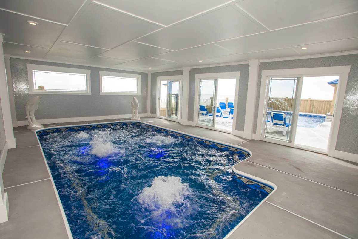 This image features an indoor swimming pool with elegant water features and large windows, allowing light to fill the tranquil space. The pool is surrounded by inviting lounge areas, creating a calming and restorative environment ideal for relaxation after a long day.