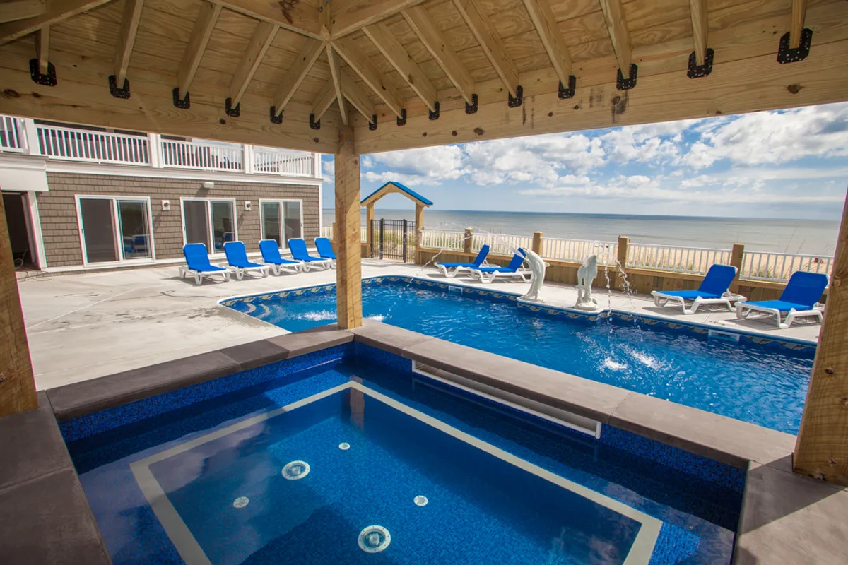 A sparkling community swimming pool surrounded by a hot tub, outdoor seating, and views of the ocean. The area is accented by lush landscaping and offers a tranquil, resort-like setting for swimming, socializing, or relaxing by the water.