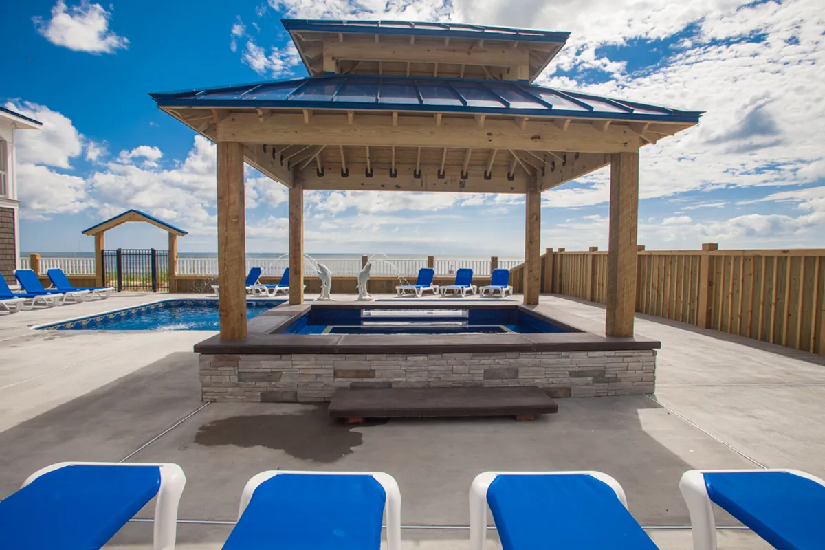 The image highlights a stylish outdoor space featuring a pergola with comfortable seating, a hot tub, and a swimming pool, all overlooking the ocean. Lounge chairs and the inviting water elements create a peaceful and private environment for relaxation.